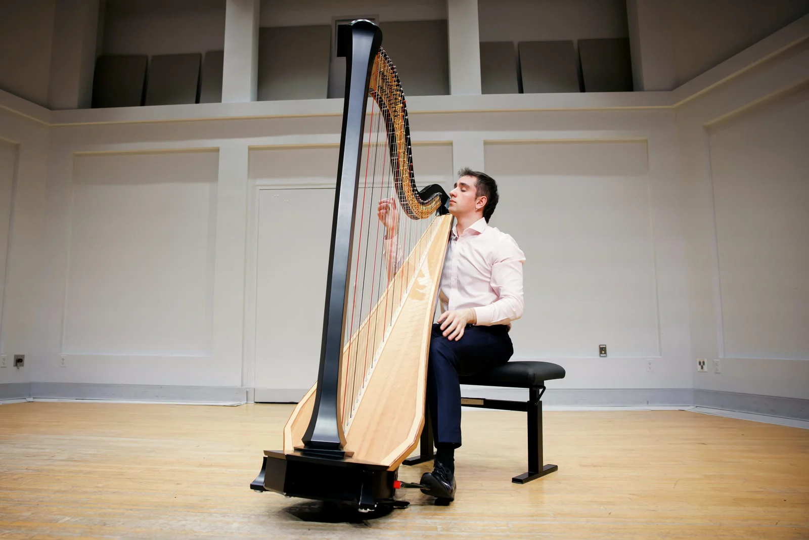 Huw Boucher seated at the harp in a bright recital hall.