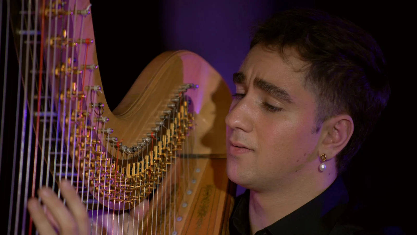 Huw Boucher in profile at the harp under stage light.