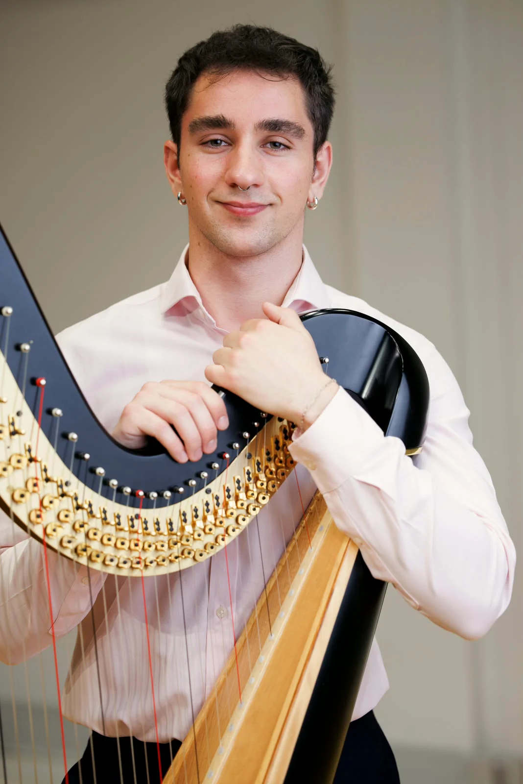 Portrait of Huw Boucher resting against a concert harp.